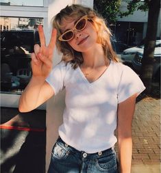 a woman in white shirt and sunglasses making the peace sign