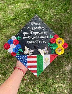 a person's hand holding a graduation cap decorated with flowers and butterflies on grass