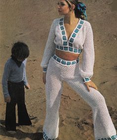 a woman standing on top of a sandy beach next to a little boy in white