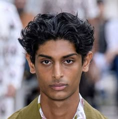 a close up of a person wearing a shirt and jacket on a street with people in the background