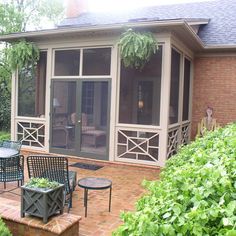 a screened in porch with chairs and tables on the brick patio next to it is surrounded by greenery