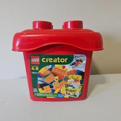 a red plastic container filled with legos on top of a white table next to a wall