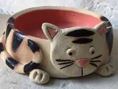 a ceramic cat sitting in a bowl on the ground