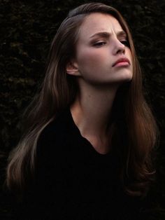 a woman with long brown hair standing in front of a bush looking up at the sky