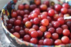 a bowl filled with red grapes sitting on top of a granite counter next to a metal spoon