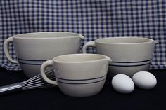 three cups and two whisks are sitting on a table with a checkered cloth