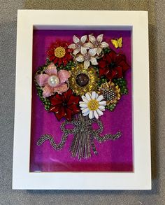 a bouquet of flowers is in a white frame on the floor next to a purple wall