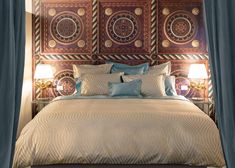 a bed with blue and white pillows in a bedroom next to two lamps on either side of the bed