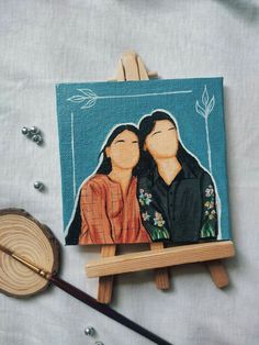 two people sitting on top of a wooden easel next to a piece of artwork