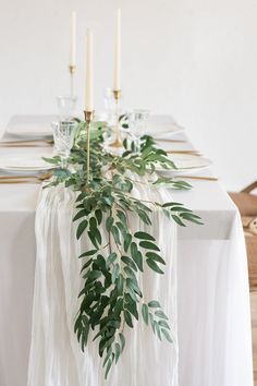 the table is set with white linens and greenery