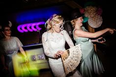 two women dressed in white are dancing at a party with one holding an umbrella and the other wearing a mask