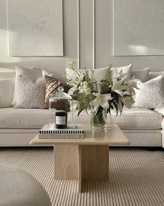 a living room with white furniture and flowers in a vase on the coffee table next to it