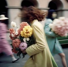 a woman is walking down the street with flowers in her hand and she's wearing a green coat