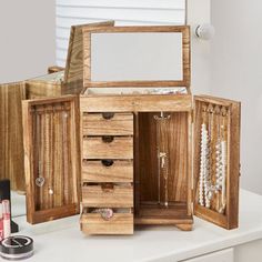 an open wooden jewelry box sitting on top of a white table next to other items