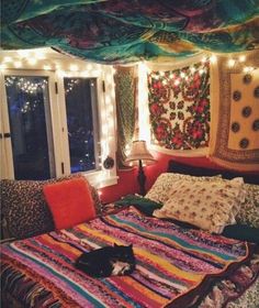 a bed covered in blankets and pillows next to a window with string lights hanging from the ceiling