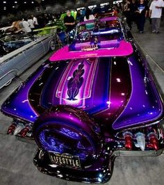 purple and black car parked on top of a parking lot next to other cars at night