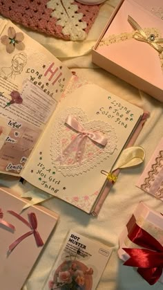 an open book with pink ribbon and bows on it next to other cards, boxes and decorations