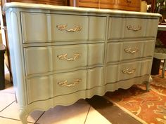 a blue dresser with gold handles on it's drawers in a room filled with furniture