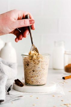 a hand holding a spoon over a jar filled with oatmeal and cinnamon