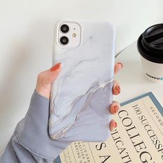 a woman holding up her phone case while sitting next to a book and coffee cup