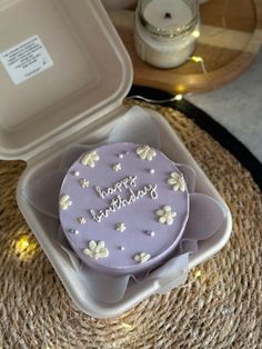 a birthday cake in a plastic container on a wicker place mat next to a candle