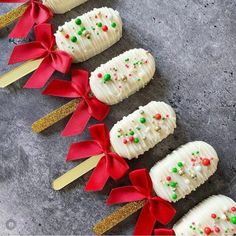 some white cake pops with red bows and green sprinkles are on a gray surface