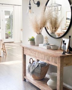 a wooden table topped with vases filled with flowers next to a wall mounted mirror