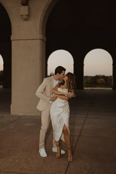 a man and woman kissing in front of arches