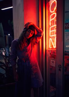 a woman standing in front of a neon sign with her hands on her head and looking at the camera