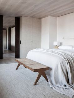 a bedroom with a large bed and white sheets on the walls, along with a wooden bench