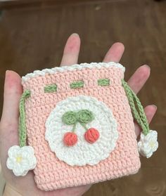 a hand holding a small crocheted pink and white bag with a clown face on it