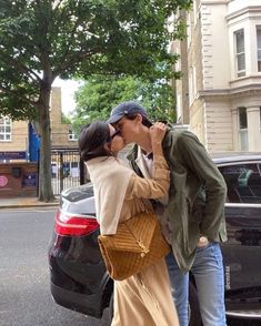 a man and woman kissing in front of a car on the side of the road