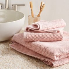 three folded pink towels sitting on top of a bathroom counter next to a white bowl