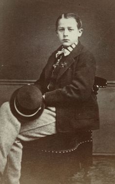 an old black and white photo of a boy in a suit sitting on a chair