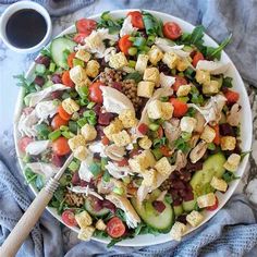 a salad with dressing and vegetables on a white plate next to a cup of coffee