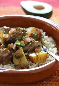 a bowl filled with rice and meat on top of a table next to an avocado