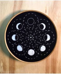 a black and white embroidery project with phases in the center on a wooden table top