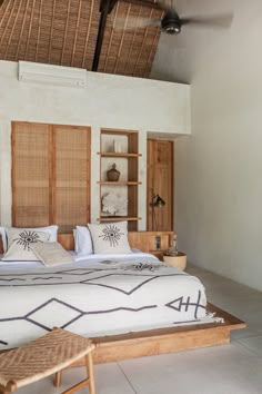 a large bed in a bedroom next to a wooden table and chair with pillows on it