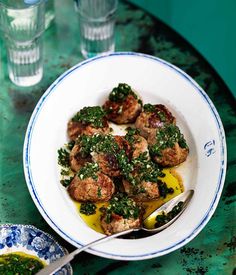 a white plate topped with meatballs covered in pesto sauce and lemon wedges