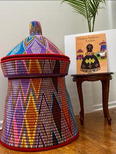 a colorful basket sitting on top of a wooden floor next to a table with a book