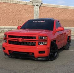 a red truck parked in a parking lot next to a building with a statue behind it