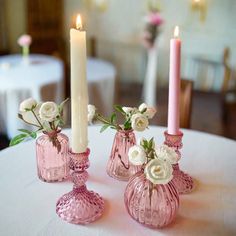 three pink vases with white flowers are sitting on a table next to two candles