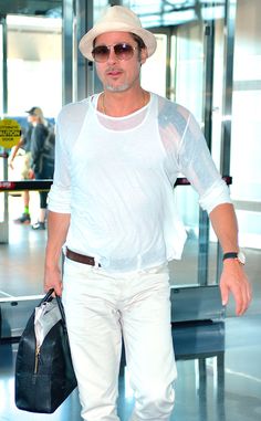 a man in white shirt and hat walking through an airport with his hand on his hip