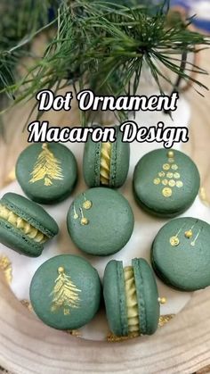 green macaroons with gold designs on them sitting in front of a pine tree