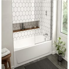 a white bath tub sitting under a window next to a wooden stool and potted plant