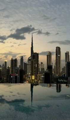 a city skyline with skyscrapers in the background and water reflecting on the ground at sunset