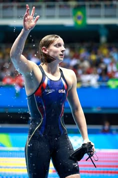 a woman in a wet suit standing on top of a swimming pool holding her hand up