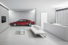 a red sports car is parked in a white room next to a couch and coffee table