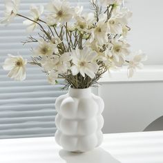 a white vase with flowers in it sitting on a table next to a window sill