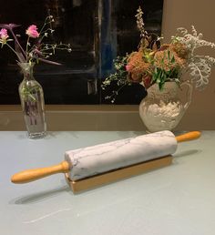 two vases with flowers in them and a rolling pin sitting on a counter top